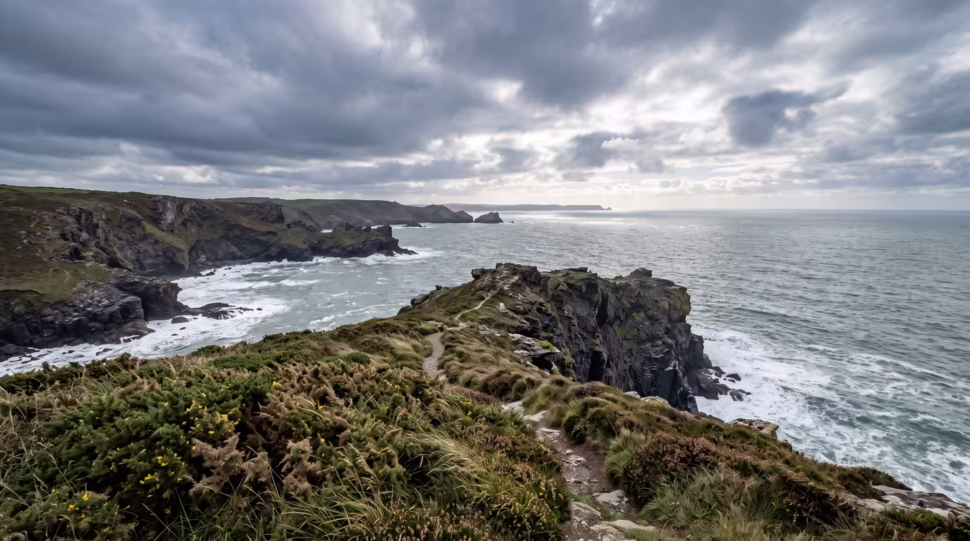 Rugged Cornish coastline with cliffs, gorse and grey-green sea under a wide sky