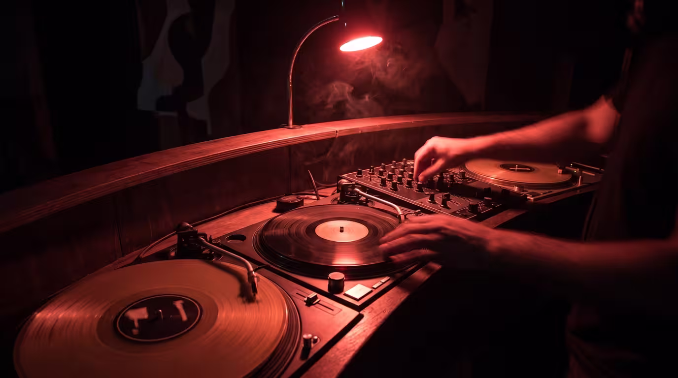 Three turntables and a mixer arranged in an arc in a dark booth, hands blurred mid-mix