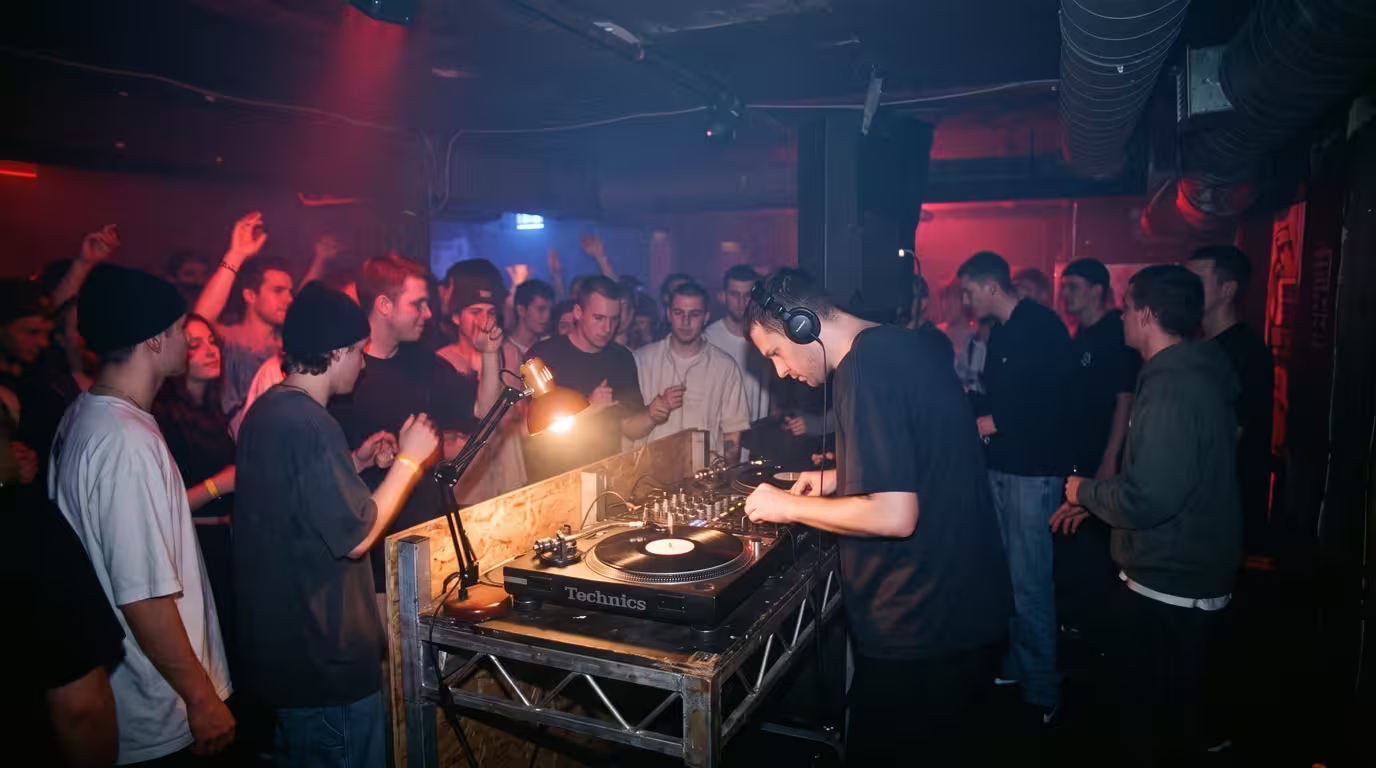 A DJ mixing vinyl in a smoky 1990s nightclub with a crowd dancing in moody light